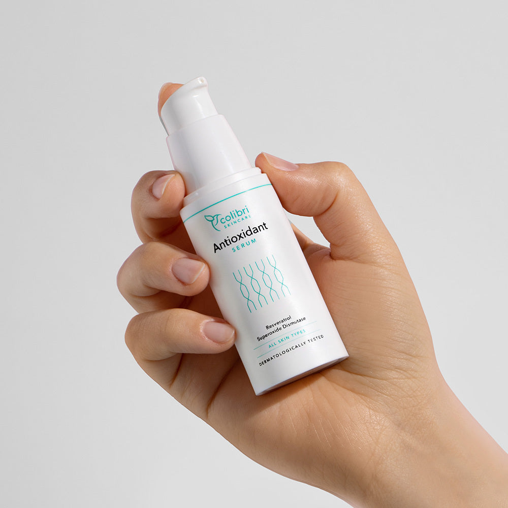 Eine Hand hält eine weiße Flasche Antioxidant Serum mit Pumpverschluss vor einem neutralen Hintergrund.