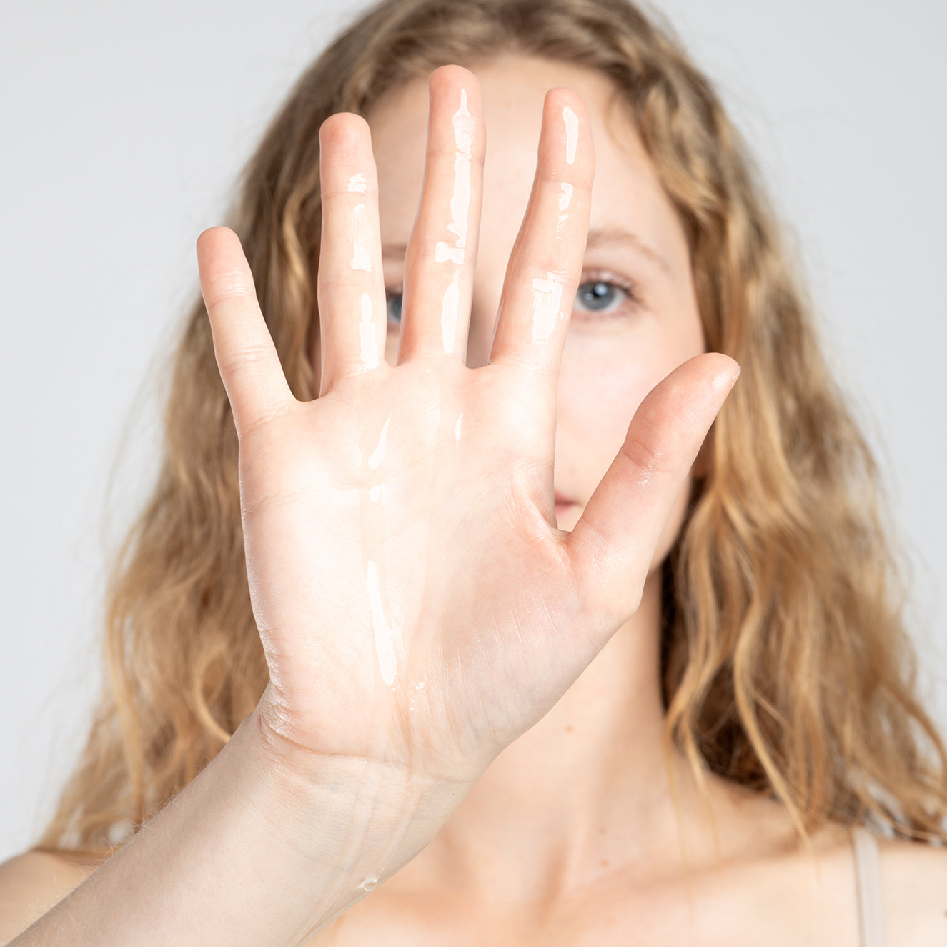Frau mit lockigem Haar hebt ihre offene Handfläche mit Gel oder Lotion vor ihrem Gesicht hoch.