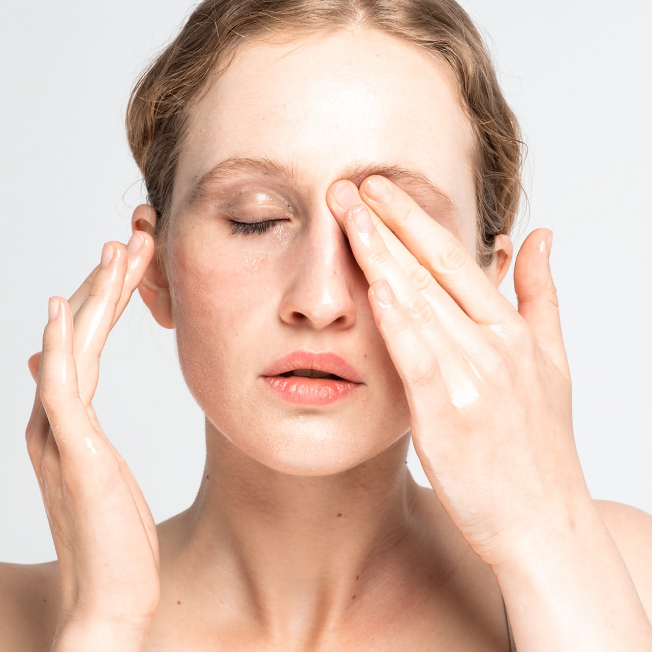 Frau mit geschlossenen Augen massiert ihr Gesicht mit beiden Händen auf weißem Hintergrund.