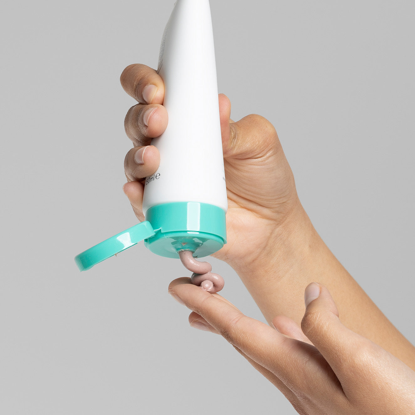 Eine Hand drückt cremefarbene Lotion aus einer weißen Tube mit türkisfarbenem Deckel auf die Fingerspitzen.