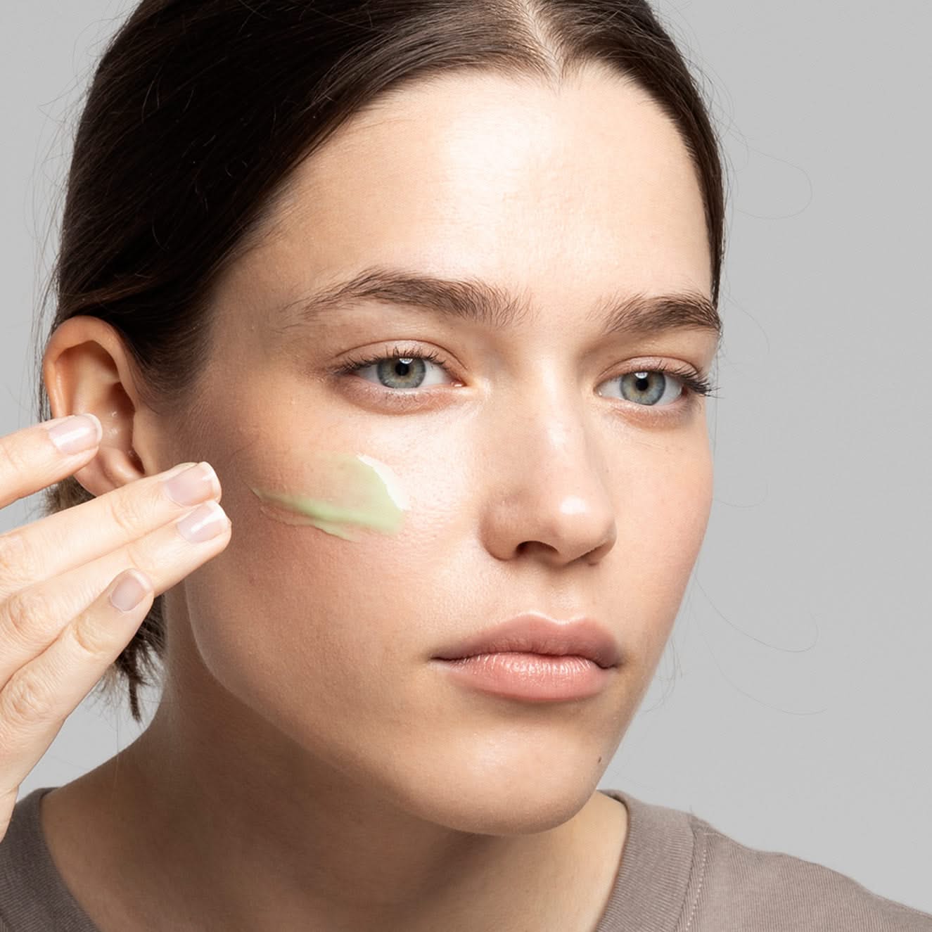 Eine Frau trägt eine grüne Creme auf ihre Wange auf.