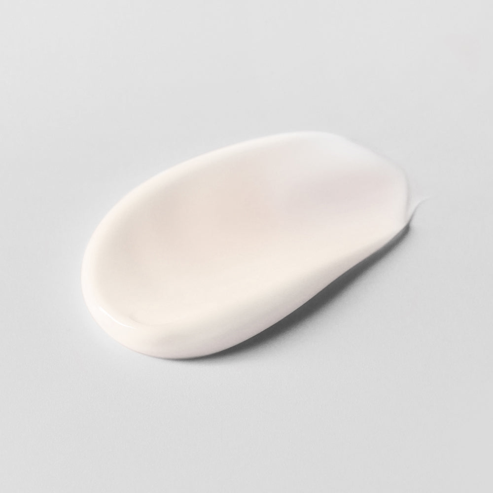 Ein ovaler Klecks weißer Creme auf einer glatten, grauen Oberfläche.