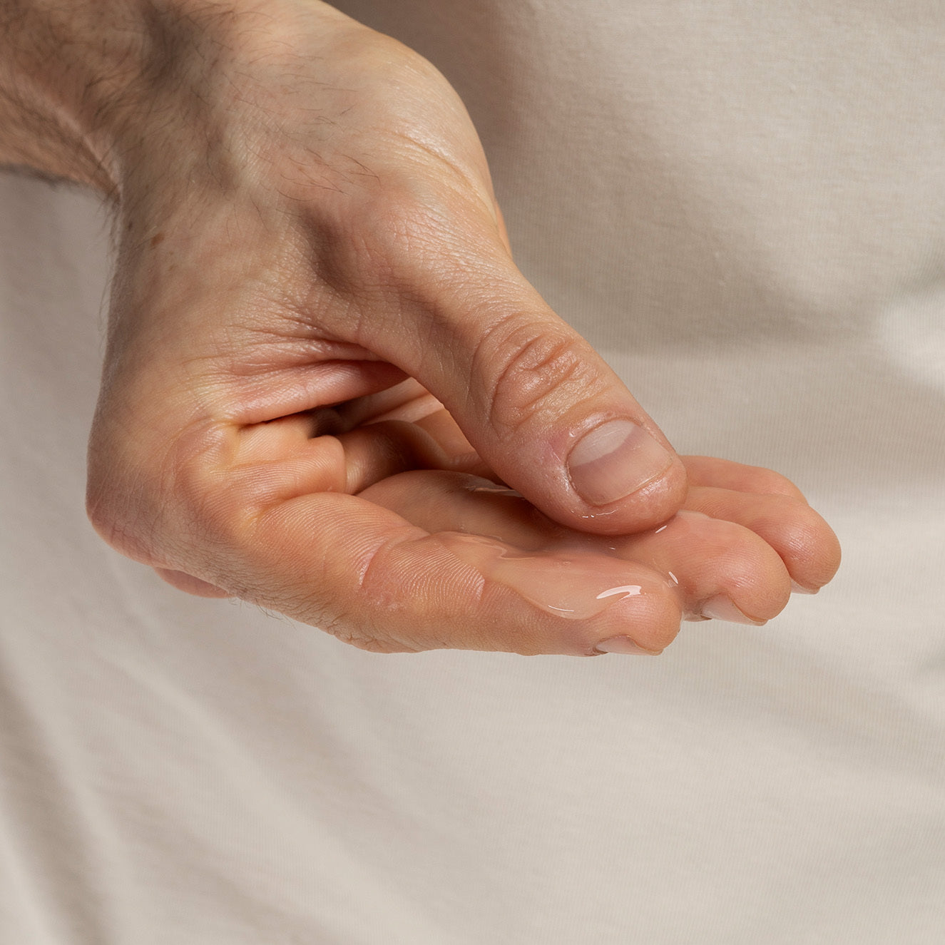 Eine geöffnete Hand hält eine kleine Menge transparenten Gels vor einem cremefarbenen Hintergrund.