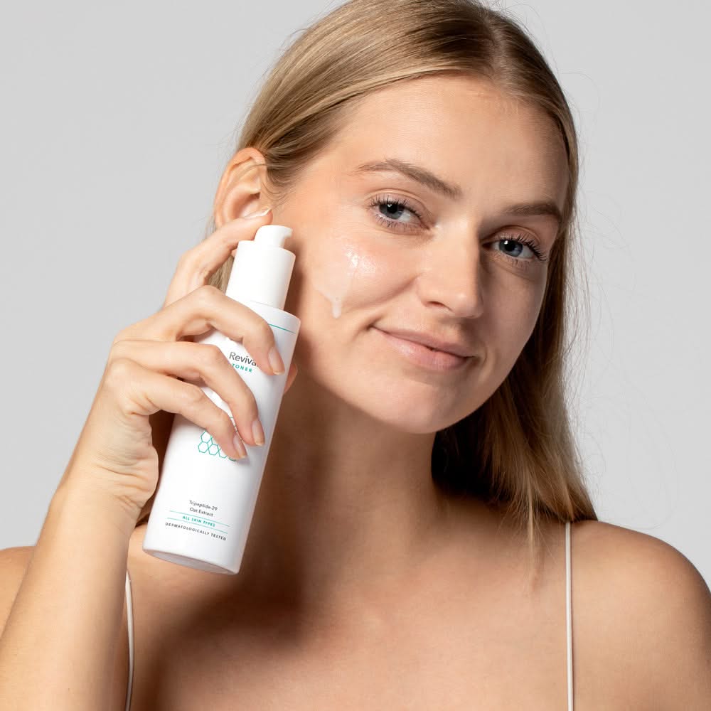 Frau trägt Hautpflegeprodukt aus weißer Flasche auf ihr Gesicht auf, mit einem Lächeln und leuchtendem Teint.