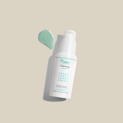Weiße Flasche mit der Aufschrift "Calming Serum" auf beigem Hintergrund mit grünem Gel neben der Flasche.