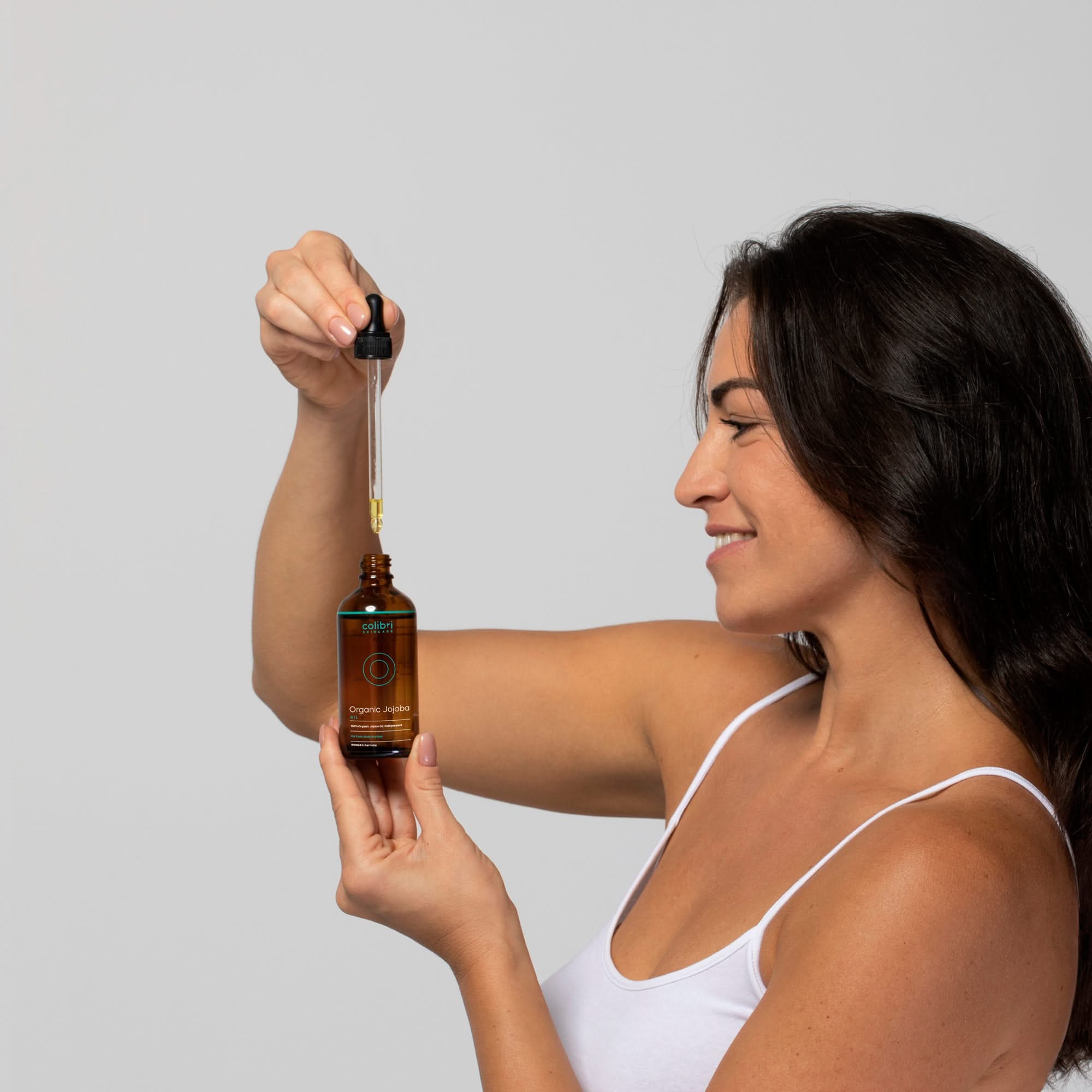 Frau in weißem Tanktop hält eine Pipettenflasche und zieht Flüssigkeit mit einer Pipette aus der Flasche auf.
