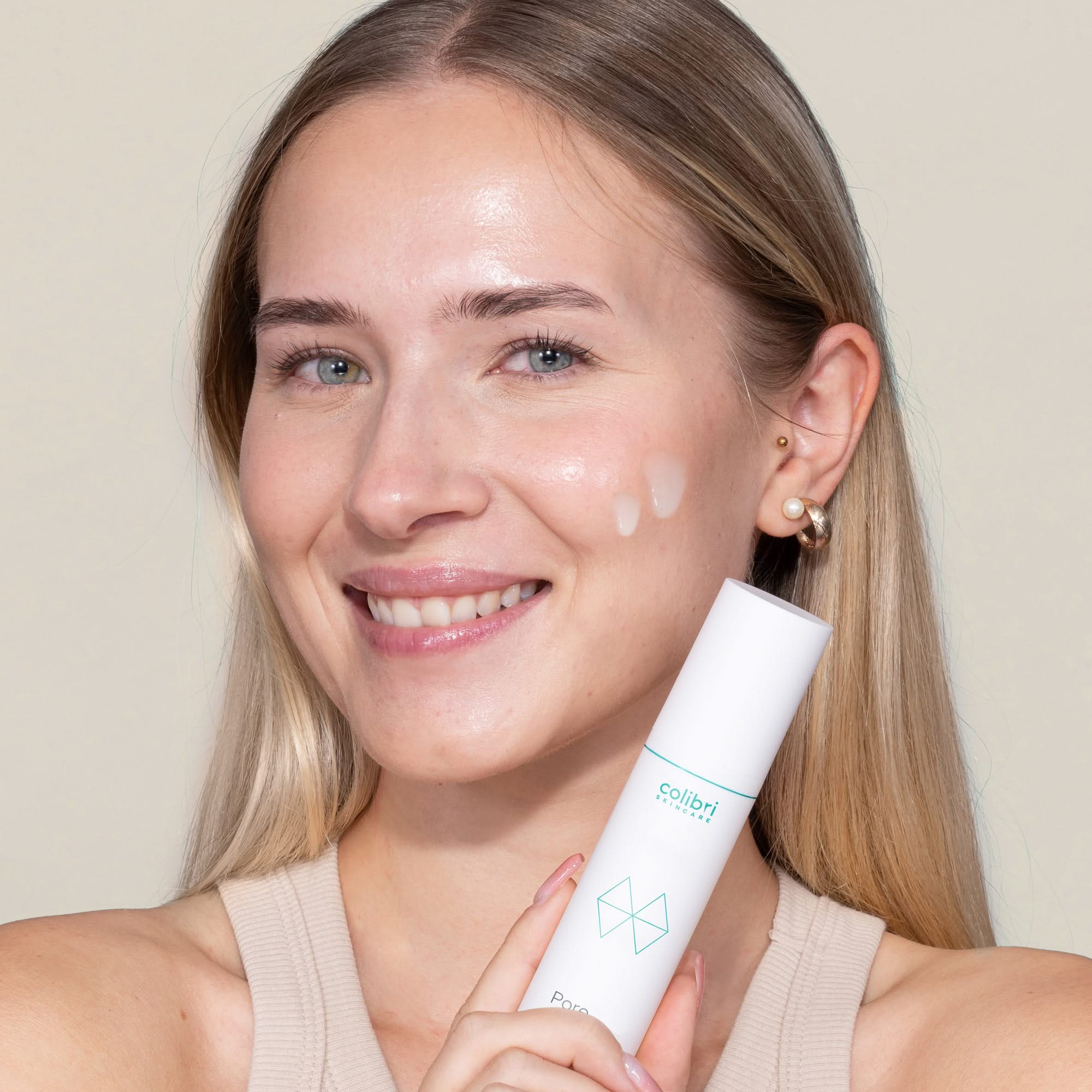 Frau lächelt in die Kamera, während sie ein Hautpflegeprodukt in der Hand hält.