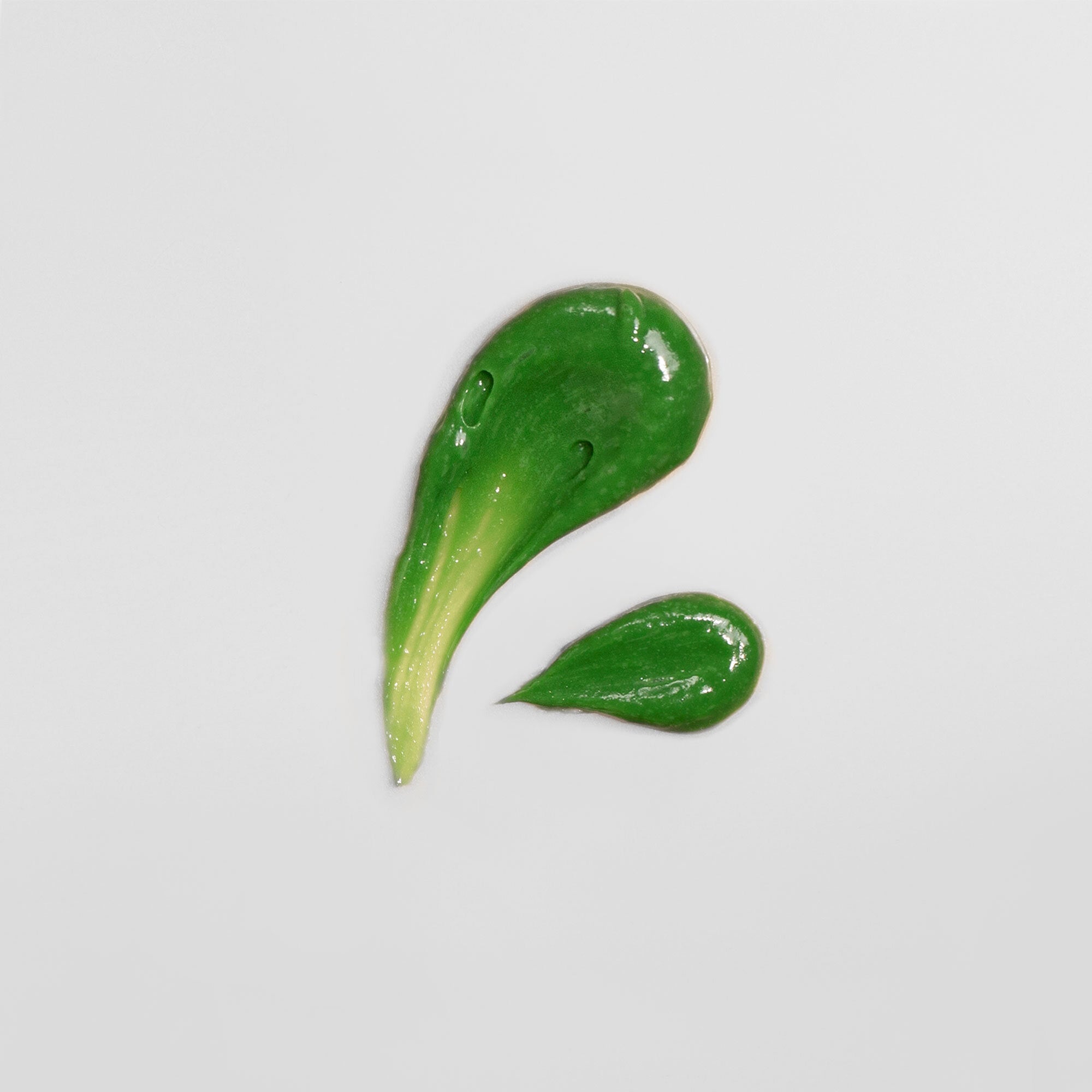 Grüne Farbkleckse auf weißem Hintergrund in tropfenähnlicher Form angeordnet.
