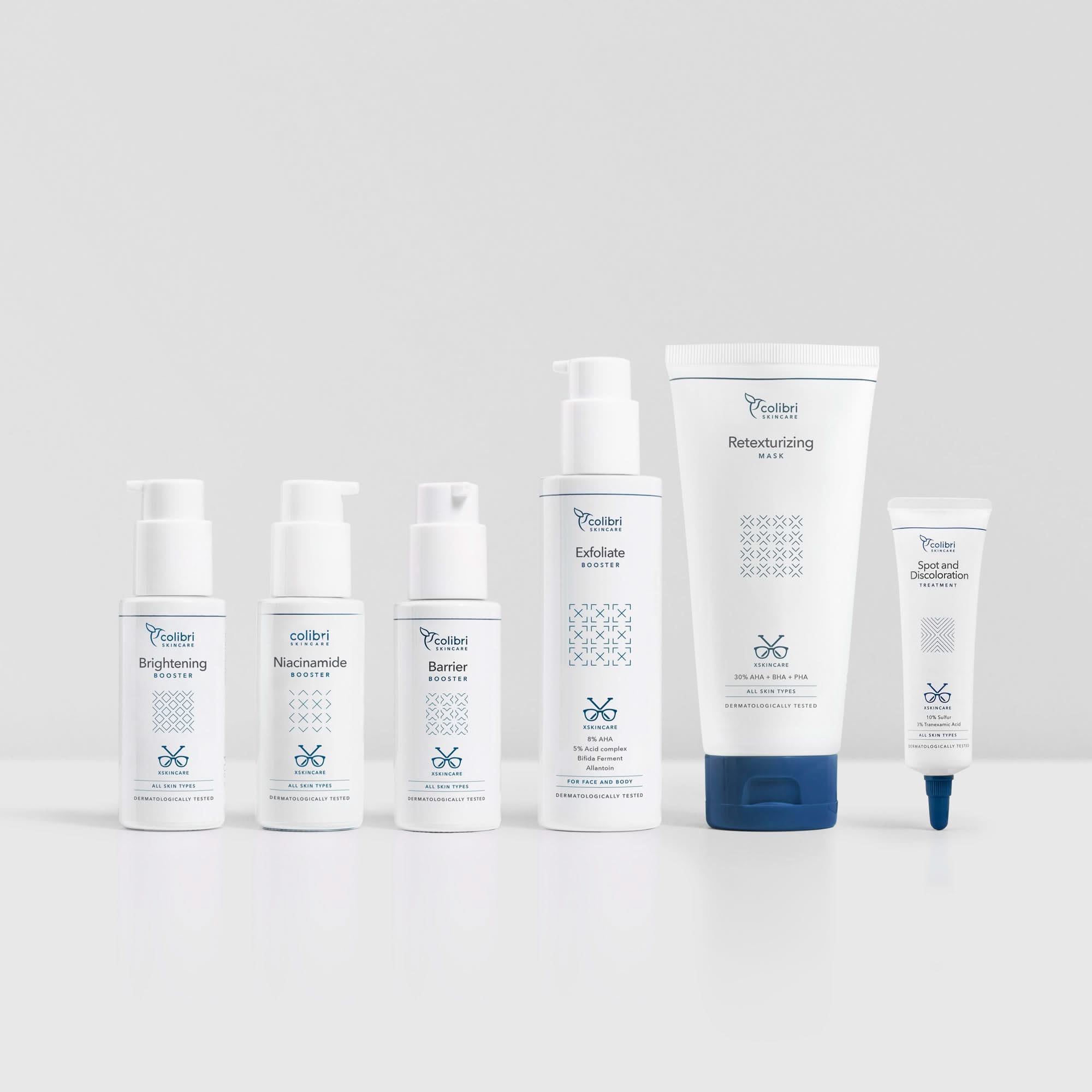 Sechs weiße Hautpflegeprodukte in verschiedenen Größen stehen nebeneinander auf einer grauen Oberfläche.