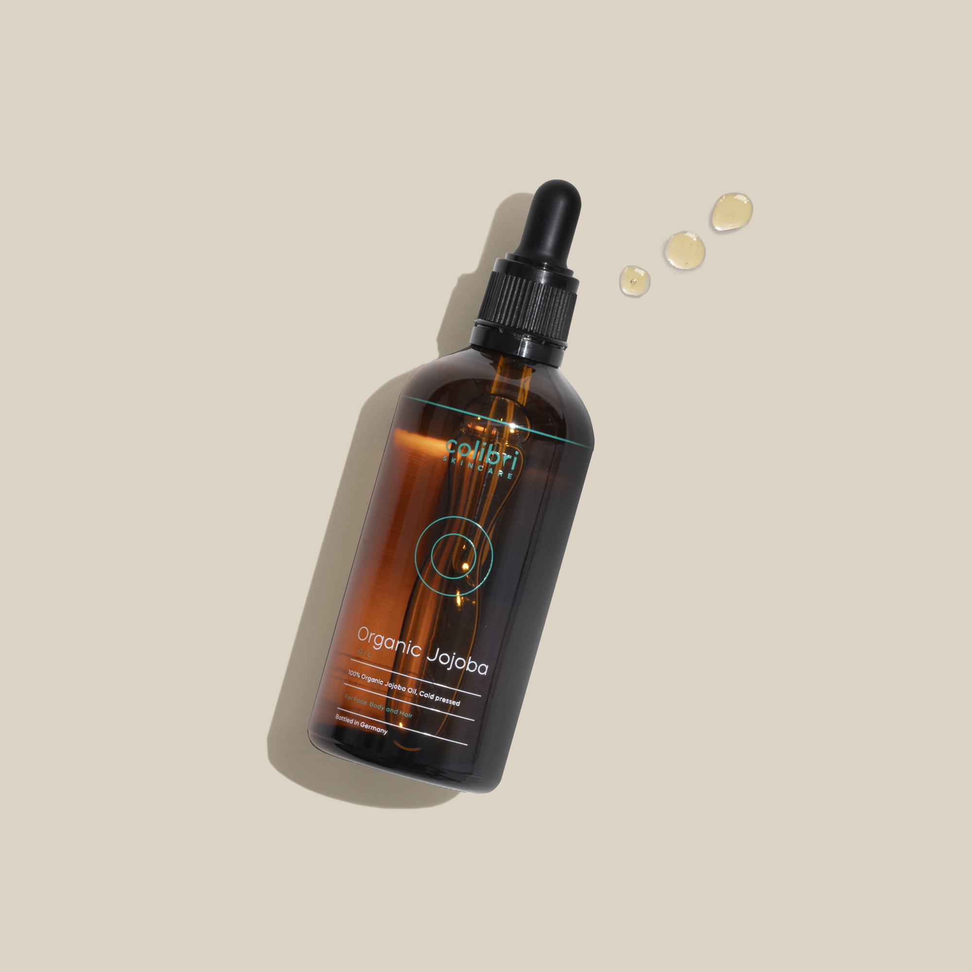 Braune Glasflasche mit Pipette, labelt "Organic Jojoba", auf hellem Hintergrund mit drei Öl-Tropfen.