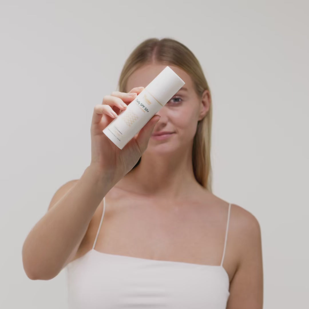 Frau in weißem Top hält eine weiße Lotionflasche vor neutralem Hintergrund in der Hand.