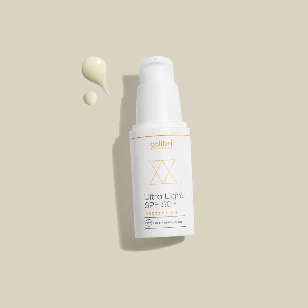 Flasche mit "Ultra Light SPF 50+"-Sonnencreme auf beigem Hintergrund, daneben zwei Kleckse der Creme.