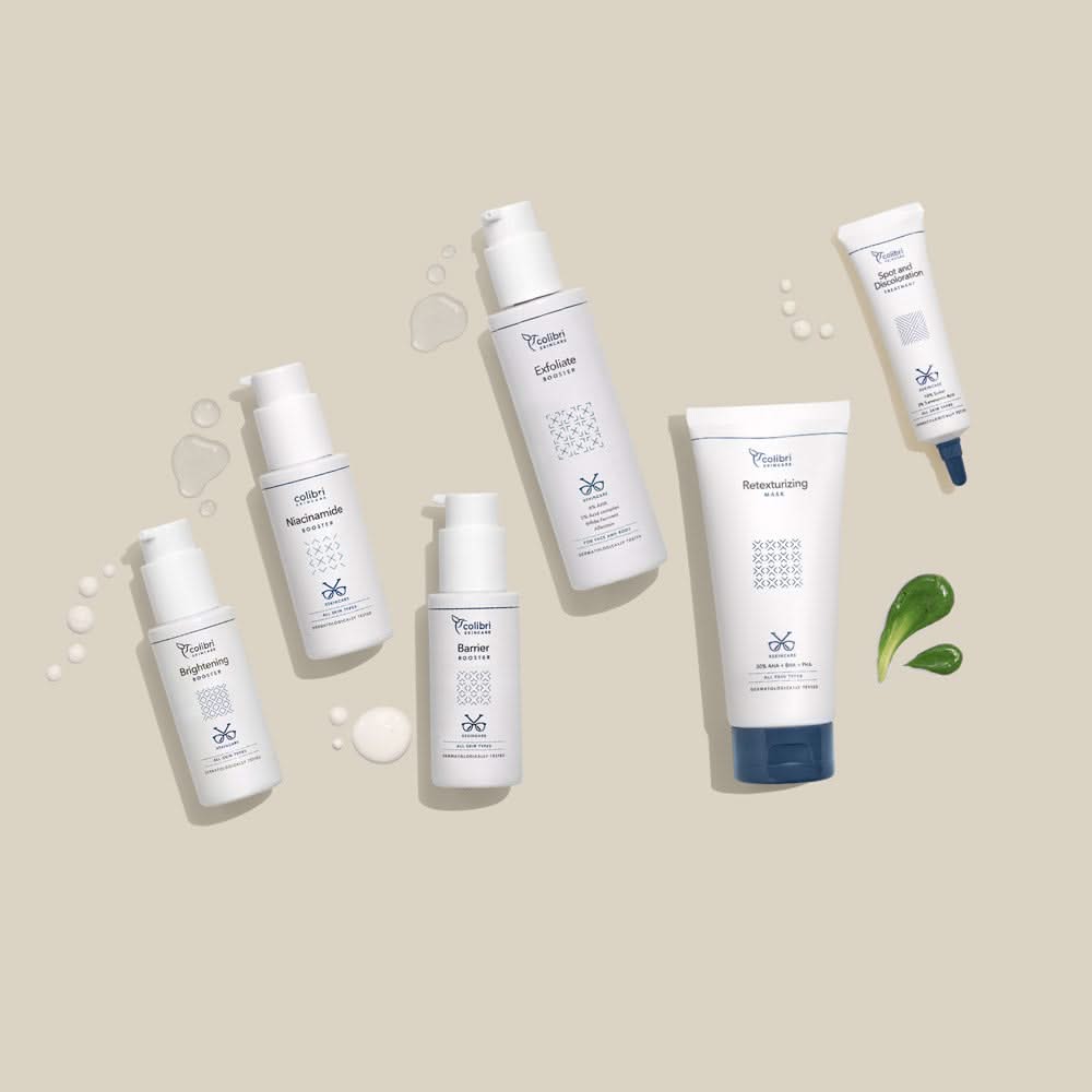 Mehrere Hautpflegeprodukte in weißen Flaschen und Tuben auf einem beigen Hintergrund mit grünen Gelklecksen.